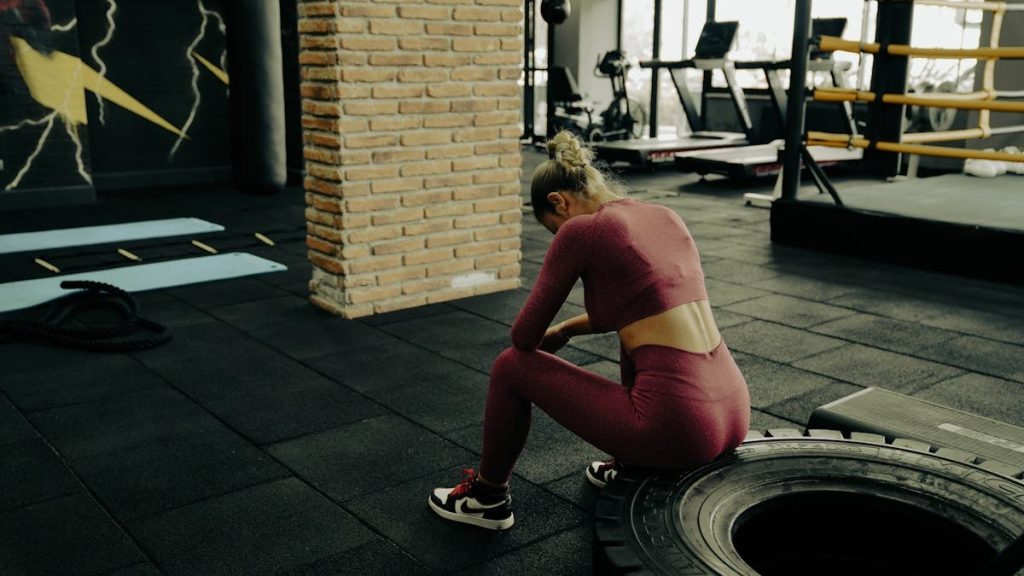 A woman in sportswear rests on a tire during gym training, showcasing fitness dedication.